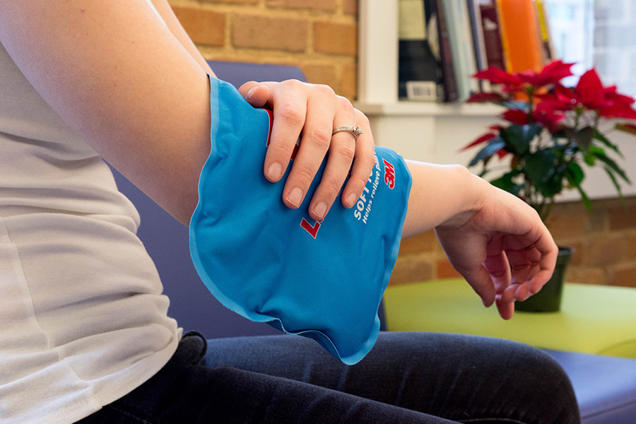 a woman holds a heat pack on her sore elbow