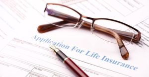glasses and a pen lie on top of life insurance paperwork
