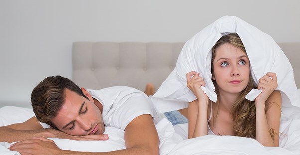 a woman holds a pillow over her head to prevent hearing her husband snoring